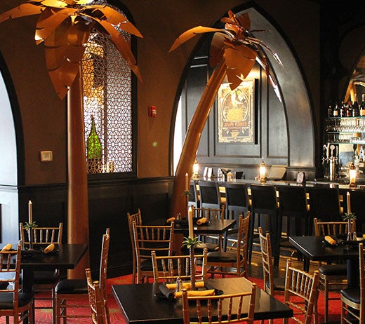 Photo of interior of Curtain Call lounge showing a bar and table seating. Two large gold palm tree sculptures are an exotic focal point.